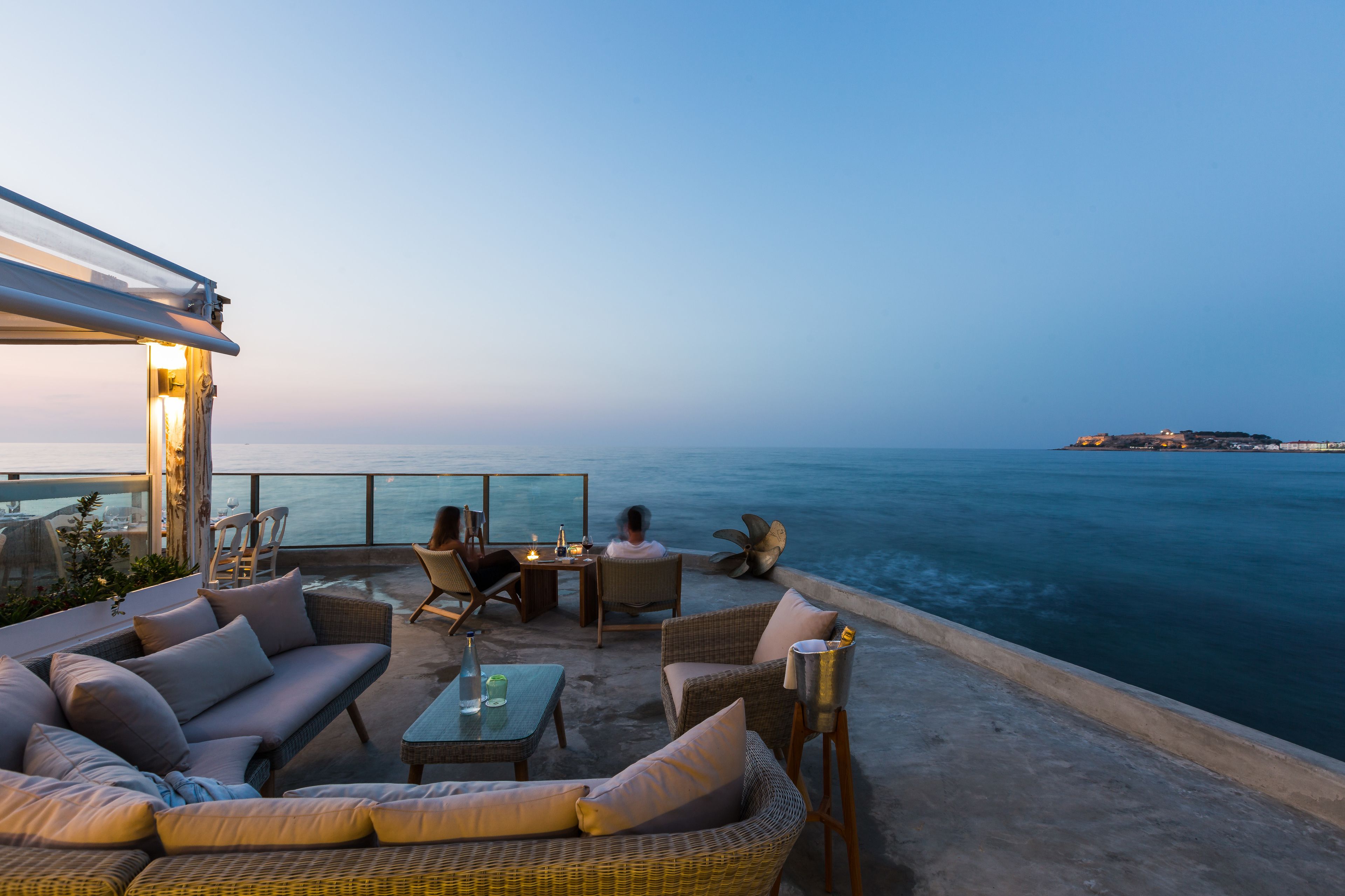 A terrace with wicker furniture, a glass table, and a view of the sea.