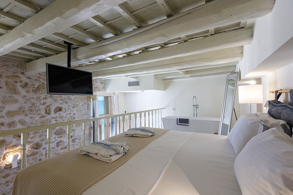Un dormitorio con cama, televisor montado en la pared y baño a la vista a través de una puerta abierta.