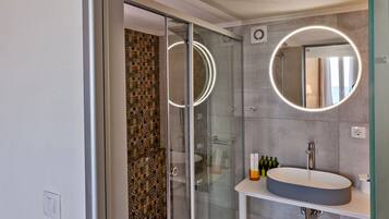 A modern bathroom with a glass shower enclosure, a round mirror, and a white sink.