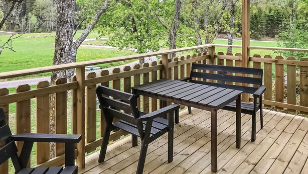 Una terraza de madera con una mesa y dos bancos, rodeada por una barandilla de madera.