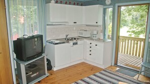 Cocina compacta con armarios blancos, microondas, cafetera y televisión.