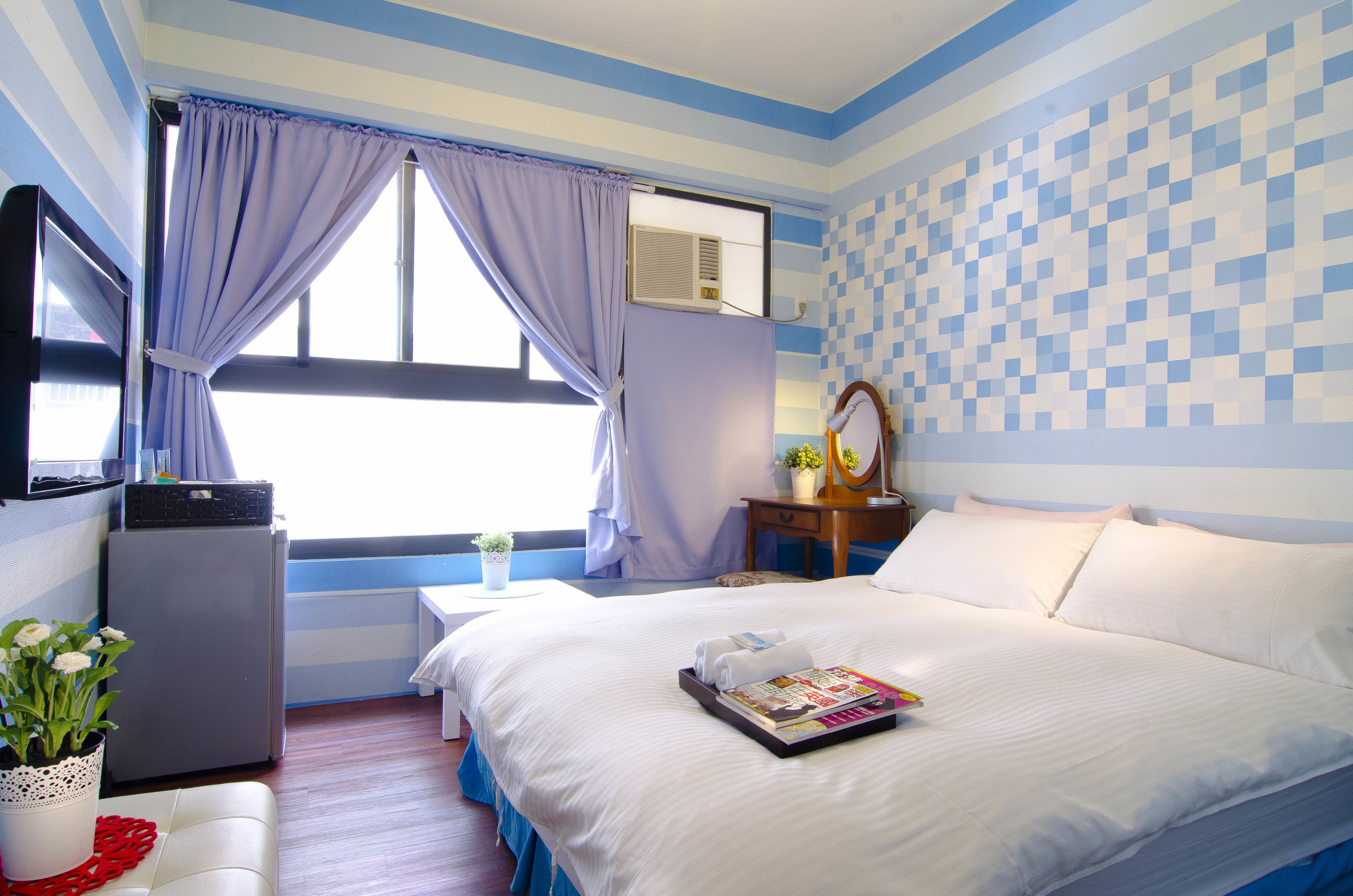 Habitación de hotel con una cama, un escritorio pequeño, un televisor y una ventana con cortinas.