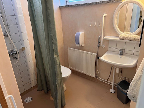 Une salle de bain comprenant des toilettes, un lavabo, un miroir, un porte-serviettes et un espace douche.