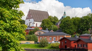 A lakeside town with historic buildings, including a church with a pointed roof and a red wooden house.