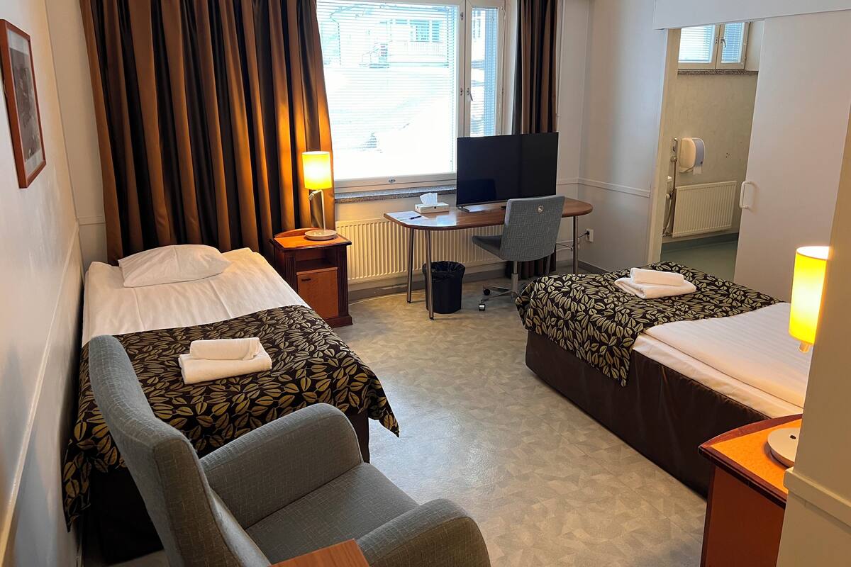 A hotel room with two beds, a desk with a computer, a chair, and a TV.