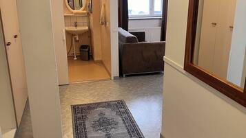 A hallway with a patterned rug, a bathroom with a sink and mirror, and a bed with a headboard.