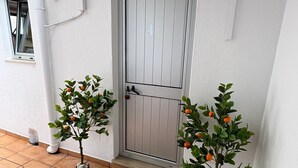 Een witte deur met daarboven een klein raam, twee plantenpotten met oranje vruchten, en een betegelde vloer.