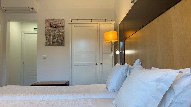 Een hotelkamer met een bed, nachtkastje, lamp, een wandplank en een deur.