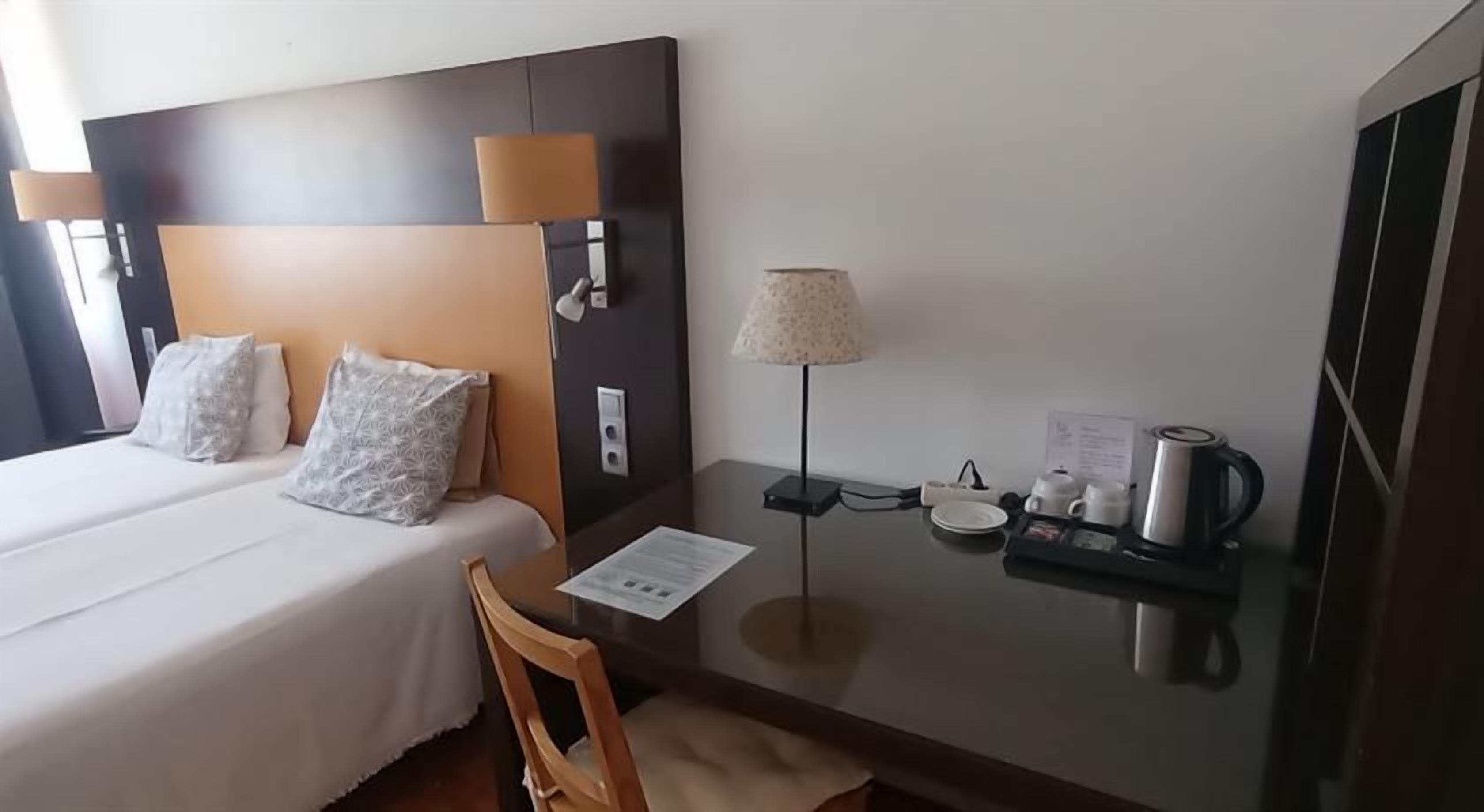 Ett hotellrum med en säng, ett nattduksbord, en lampa och ett litet skrivbord med en stol.