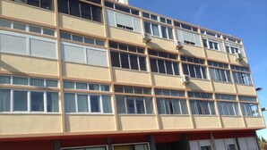 Een meerlaags gebouw met een beige gevel, grote ramen en airconditioningsinstallaties.