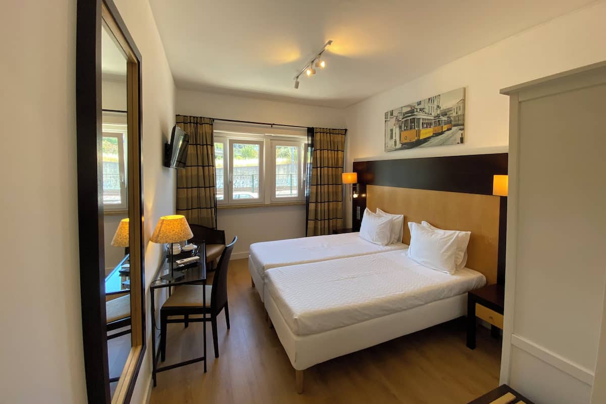 Una habitación de hotel con cama, escritorio, silla y televisor montado en la pared.