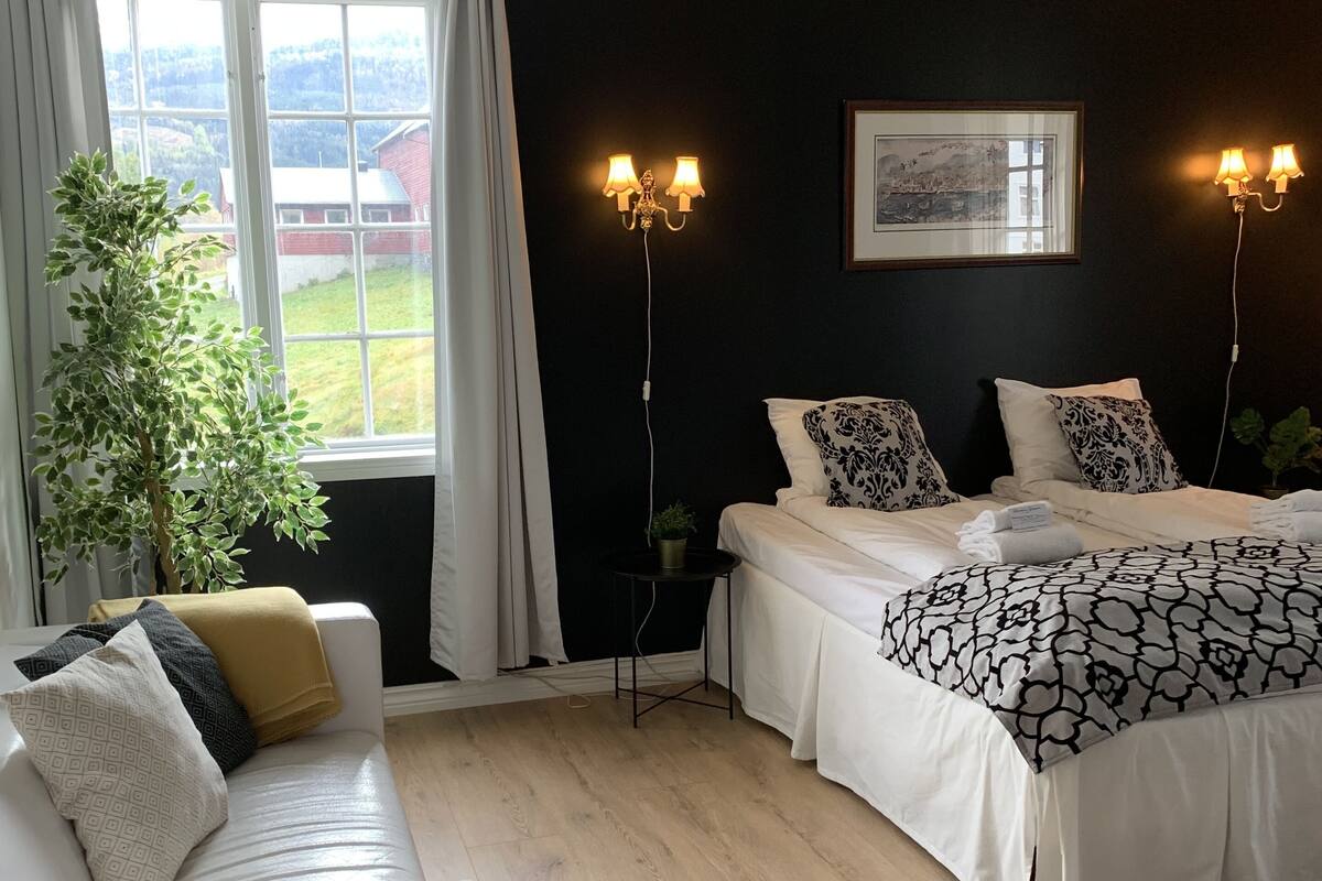 Un dormitorio con cama, sofá blanco, mesita y planta en maceta.