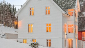 A large, multi-story white building with multiple windows and a sloped roof, surrounded by snow. - Lilandtunet Apartments Voss (Voss)