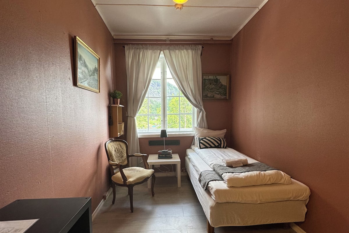Una habitación pequeña y acogedora con cama, una silla, un escritorio y una ventana con cortinas.