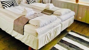 A neatly made double bed with white linens and striped pillows, a bedside table with a lamp, and a window with curtains. - Lilandtunet Apartments Voss (Voss)