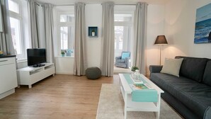 Un salon moderne avec un téléviseur, un canapé et une table sur laquelle se trouve un magazine.