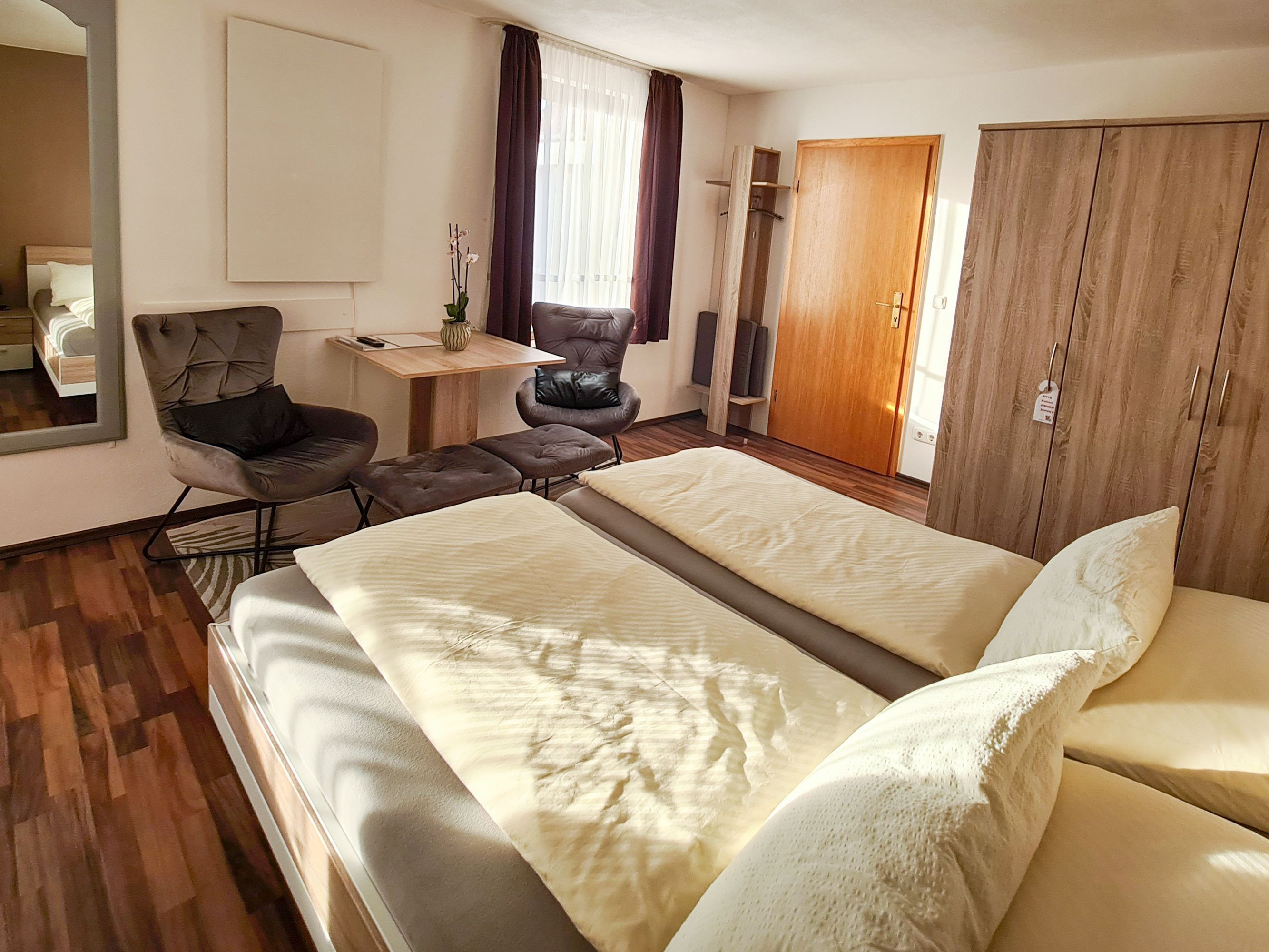 A hotel room with a bed, a chair, a desk, a wardrobe, and a mirror.