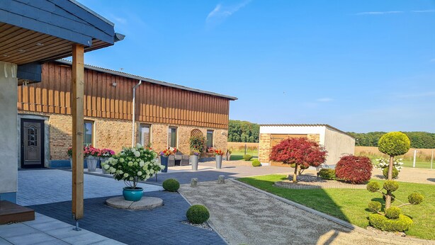 A building with a brick facade, a covered patio area, and a well-maintained garden with various shrubs and potted plants.
