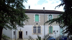 A two-story building with a white facade, green shutters, and a small front entrance with steps. - Le Parc aux Cèdres (Laroque)