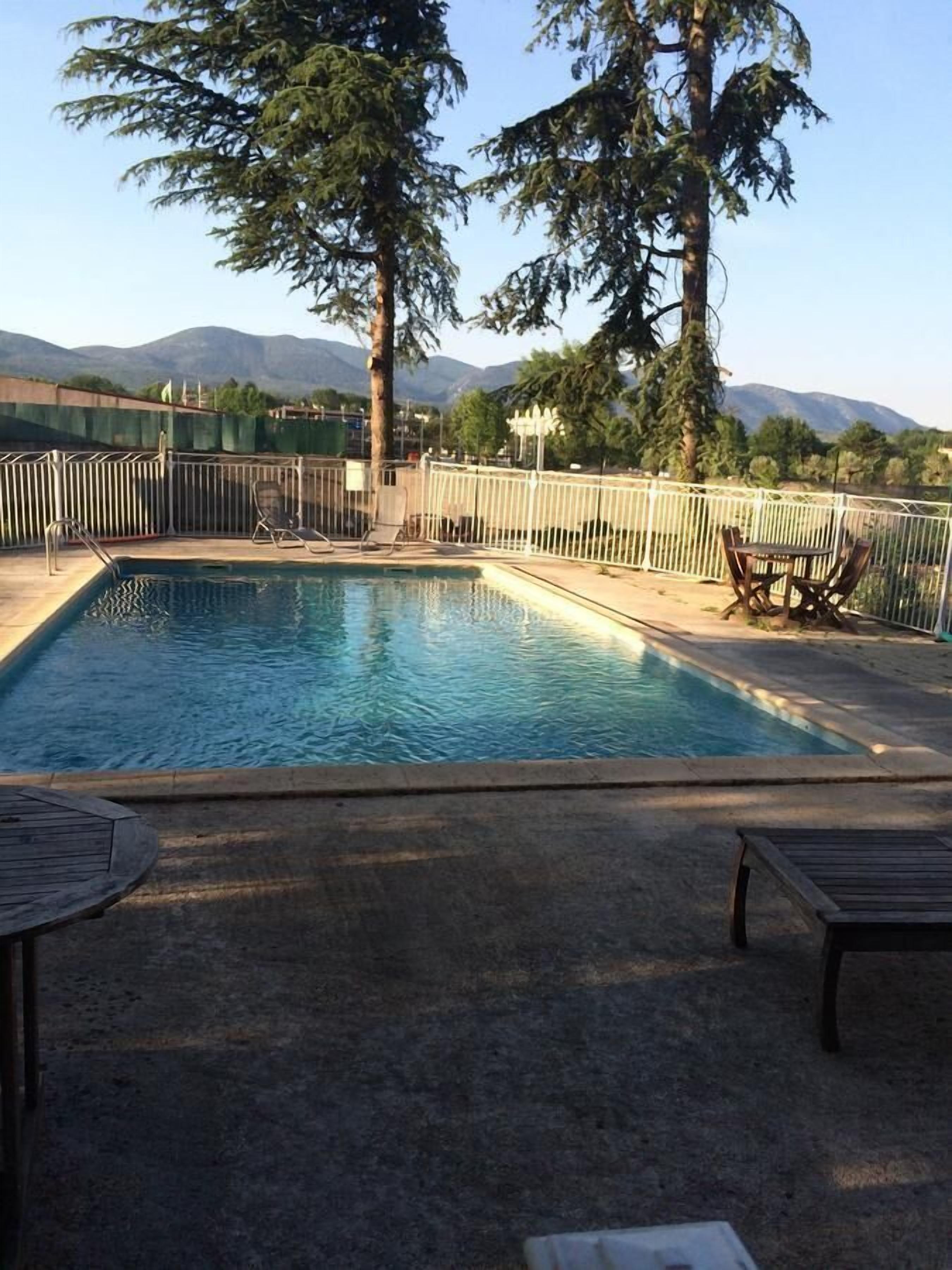 Piscina rectangular con una cerca blanca, rodeada de sillones y una mesa.