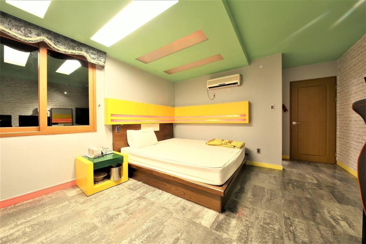 A bedroom with a bed, a bedside table with a phone, a small cabinet, and a window.