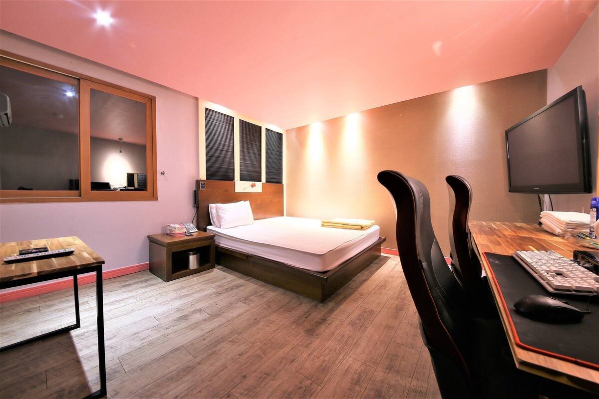 A hotel room with a bed, bedside table, desk with computer, chair, and a large mirror.