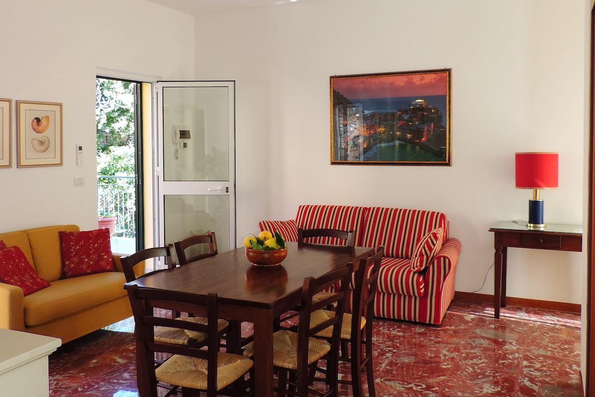 A dining area with a wooden table and chairs, a red and white striped sofa, and a cityscape painting on the wall.