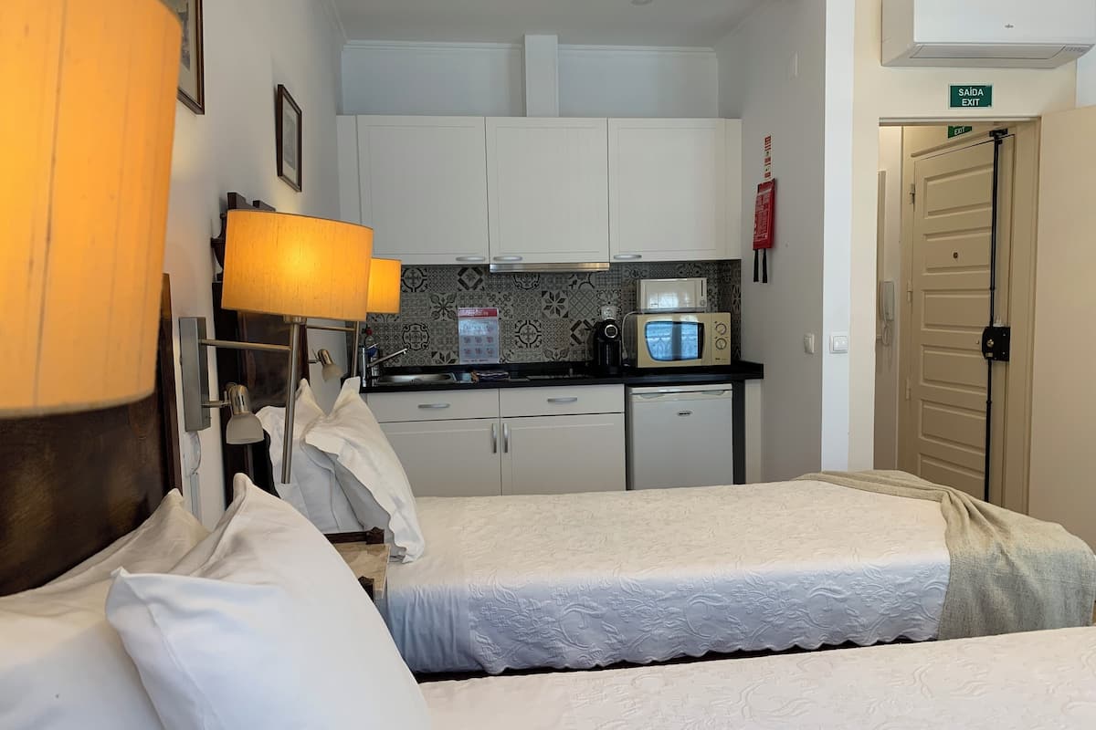 Habitación de hotel con dos camas, kitchenette, lámpara, microondas y puerta con letrero de salida.