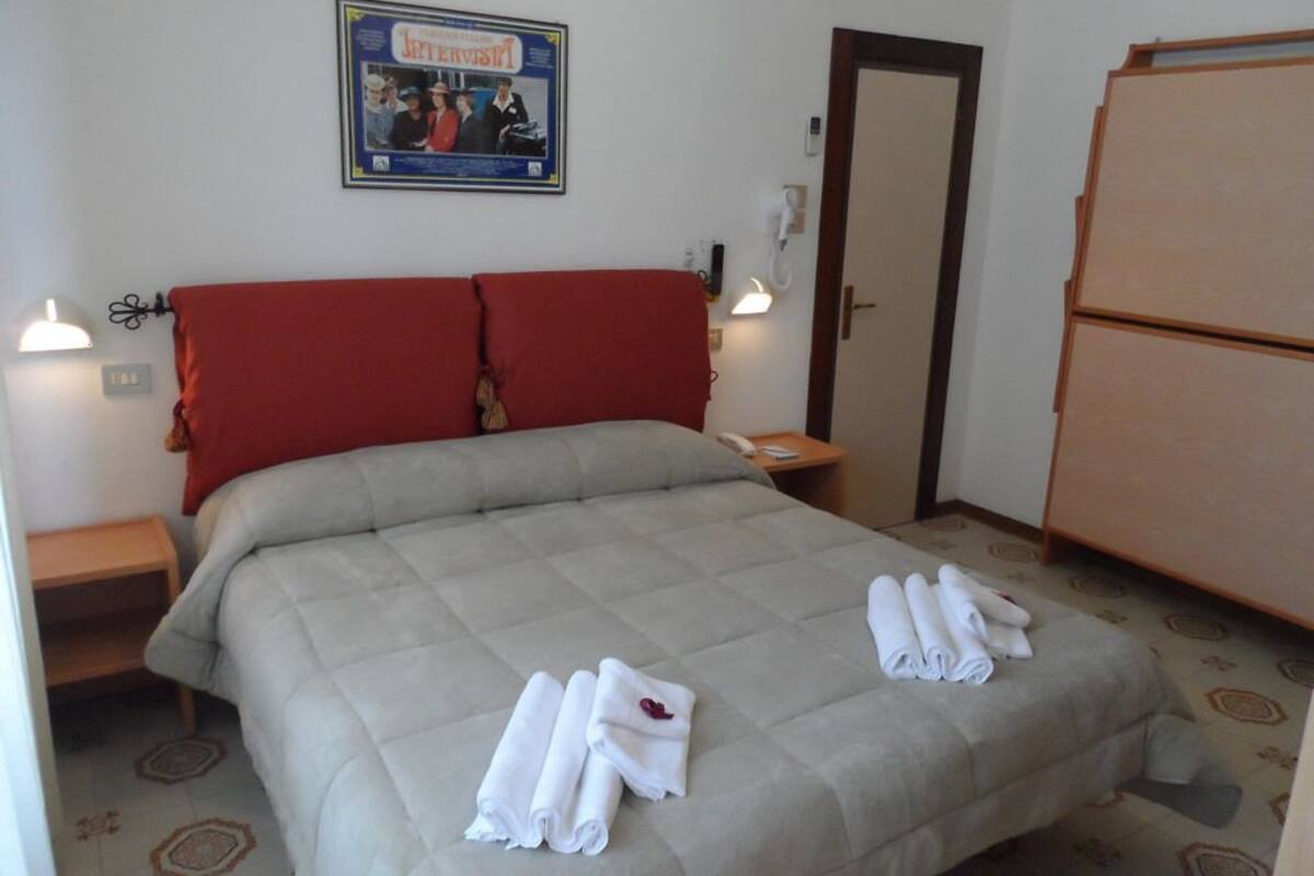Ein Hotelzimmer mit einem Bett, zwei roten Kissen, einem Nachttisch mit Telefon und einem an der Wand hängenden Poster.
