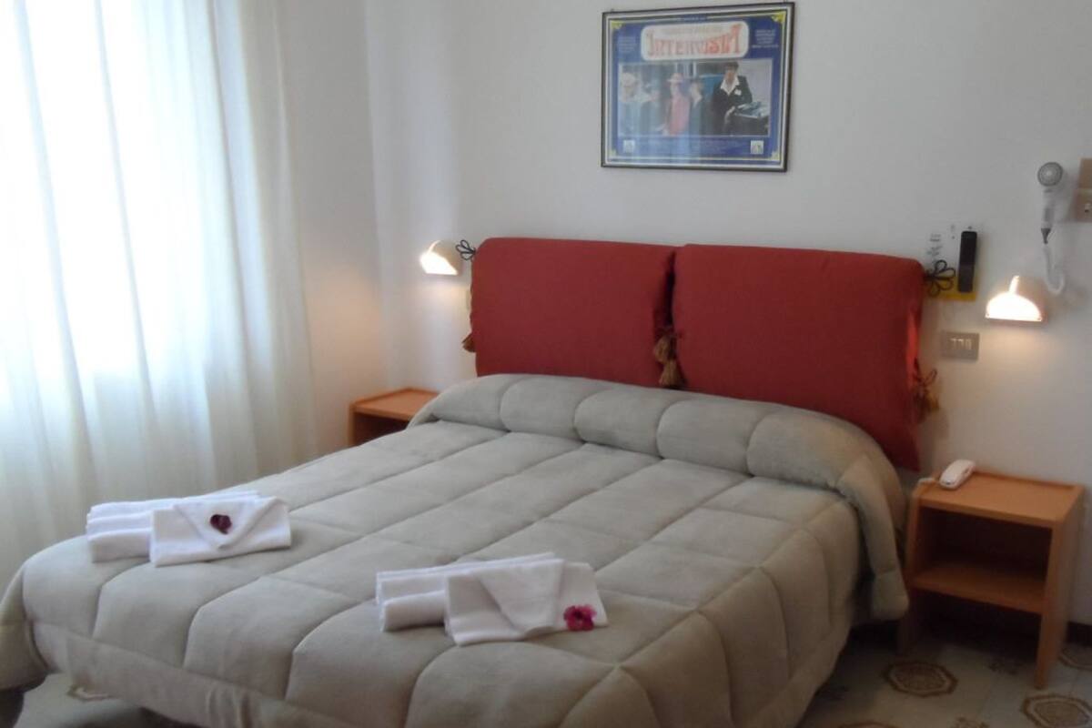 Ein Hotelzimmer mit einem großen Bett, einem roten Kopfteil, zwei Nachttischen und einem gerahmten Bild an der Wand.