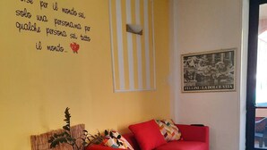 Ett vardagsrum med två röda soffor, ett svart soffbord och en randig matta. Ett citat syns på väggen, och en inramad tavla hänger ovanför soffan.