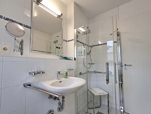 Un bagno moderno con doccia vetro, lavabo bianco con rubinetto cromato e uno specchio grande sopra il lavabo.