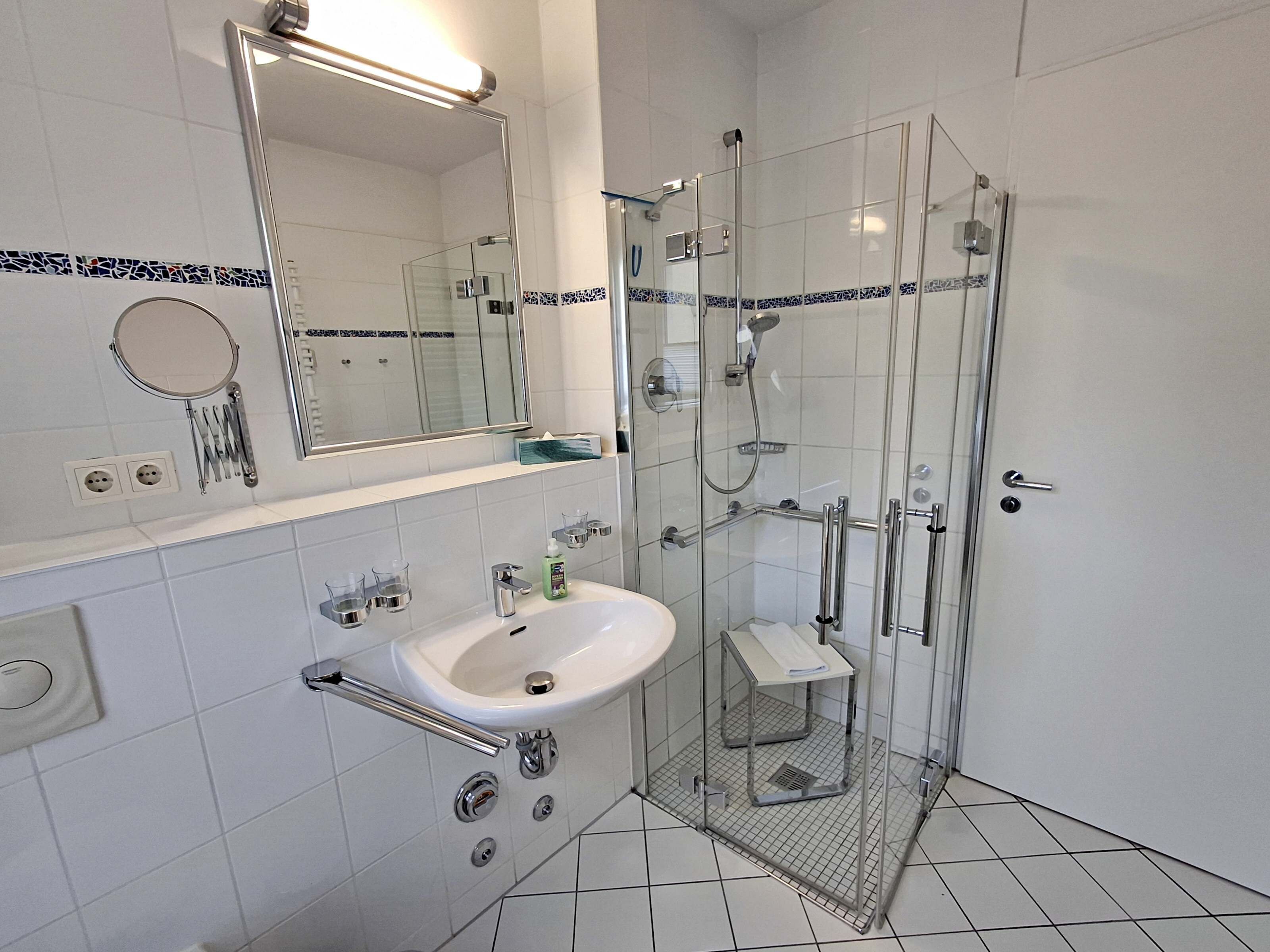 Een moderne badkamer met een douchecabine van glas, een wit wastafelmeubel met spiegel erboven, en een klein plankje met toiletartikelen.