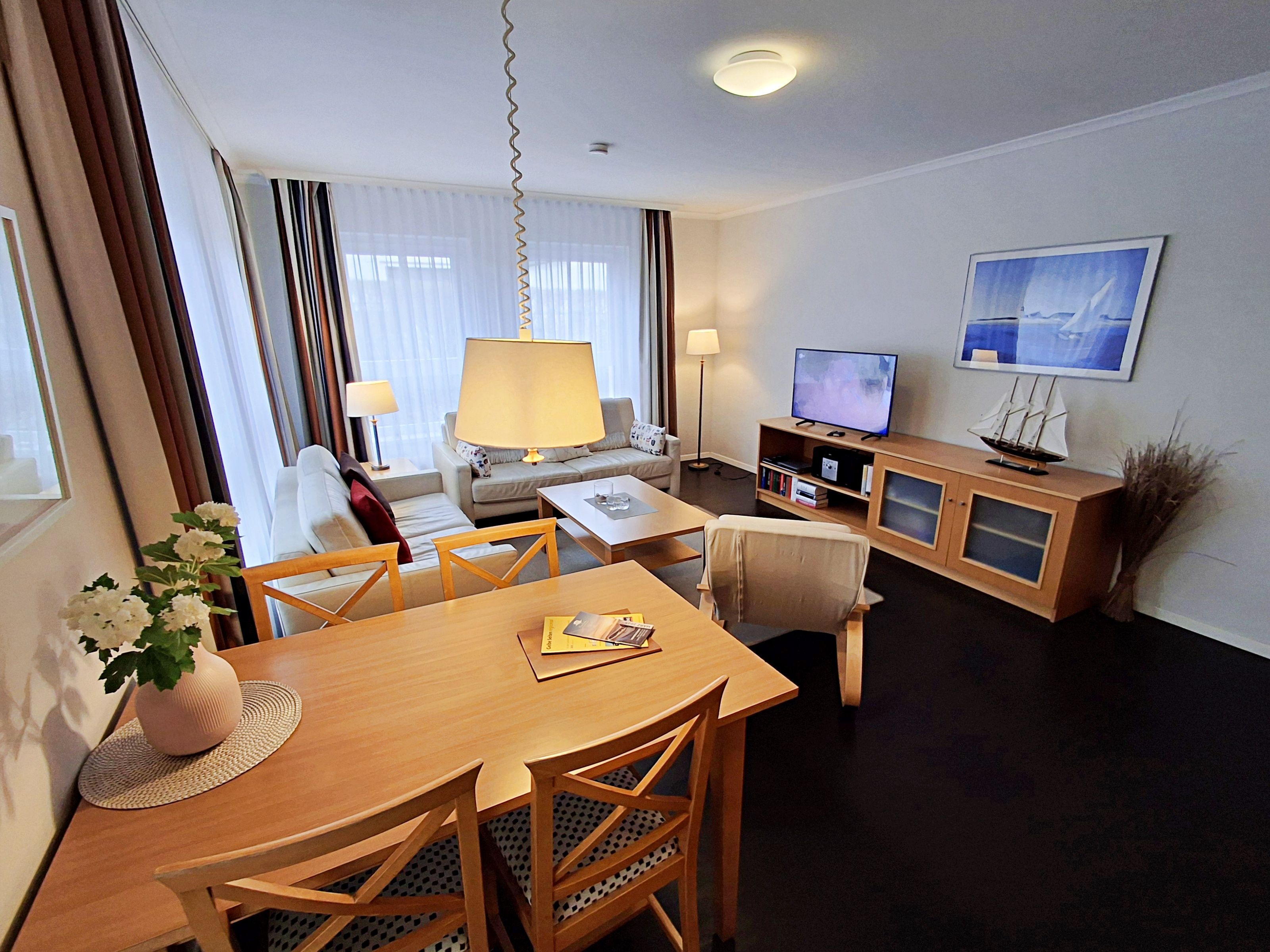 Ein Hotelzimmer mit Esstisch, Stühlen, einer Couch, einem Fernseher und einem Bücherregal.