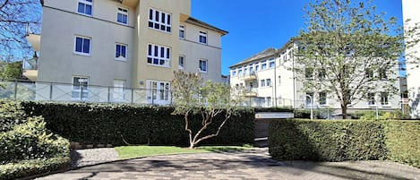 Ein mehrgeschossiges Wohngebäude mit einem gepflasterten Innenhof, umgeben von Hecken und Bäumen.
