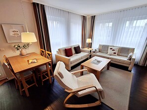Quarto de hotel com uma mesa de jantar, dois sofás, uma cadeira de balanço e um abajur.