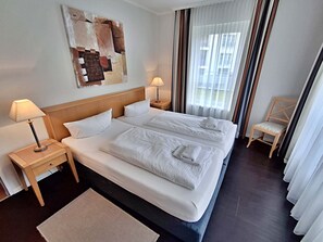 Una camera d'albergo con un letto grande, due comodini con lampade, una sedia in legno e una finestra con tende.