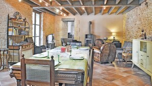 A rustic dining area with a stone wall, wooden beams, and a fireplace.