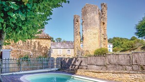 A stone building with a swimming pool, surrounded by a wooden fence and trees.