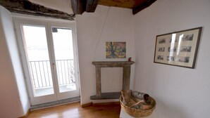 A room with wooden flooring, a fireplace, a balcony door, and a framed picture on the wall. - Casa la Finestra sul Lago - WelcHome (Cannobio)