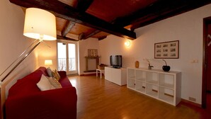 A living room with a red sofa, a TV on a white cabinet, wooden flooring, and a ceiling with exposed beams. - Casa la Finestra sul Lago - WelcHome (Cannobio)