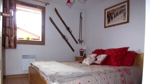 A bedroom with a wooden bed, a window with curtains, a wall-mounted ski rack, and a framed picture. - C202 - 42 m2 - 2P+Cab - 4/6 pers (Prapoutel)