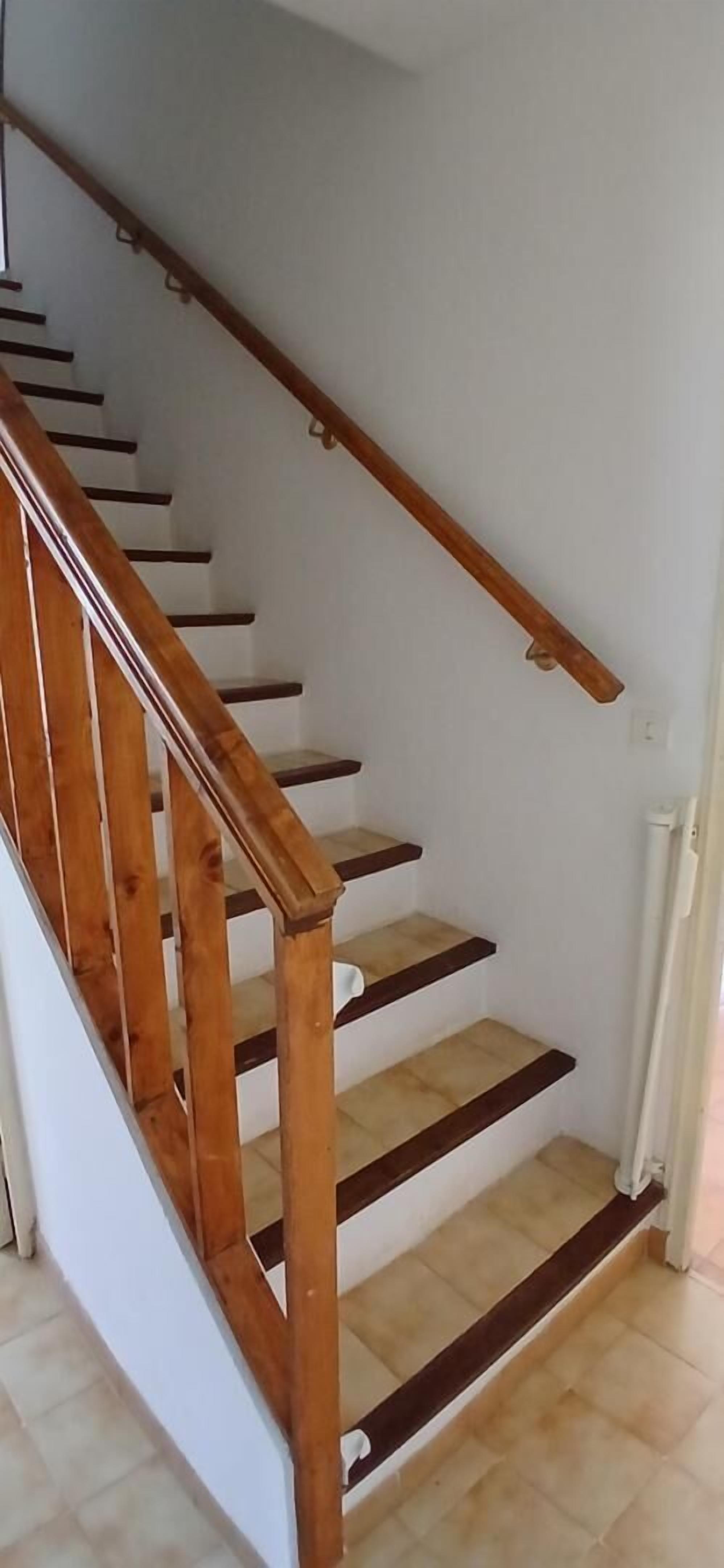 Una escalera de madera con paredes blancas y piso de baldosas.