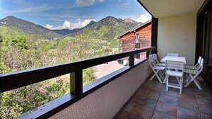 Een balkon met uitzicht op bergen en een houten gebouw. Er staat een tafel en stoelen op het balkon.