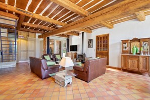 A spacious living area with a high wooden ceiling, a fireplace, leather sofas, and a tiled floor. - Homerez - Villa in Uchaux (Uchaux)