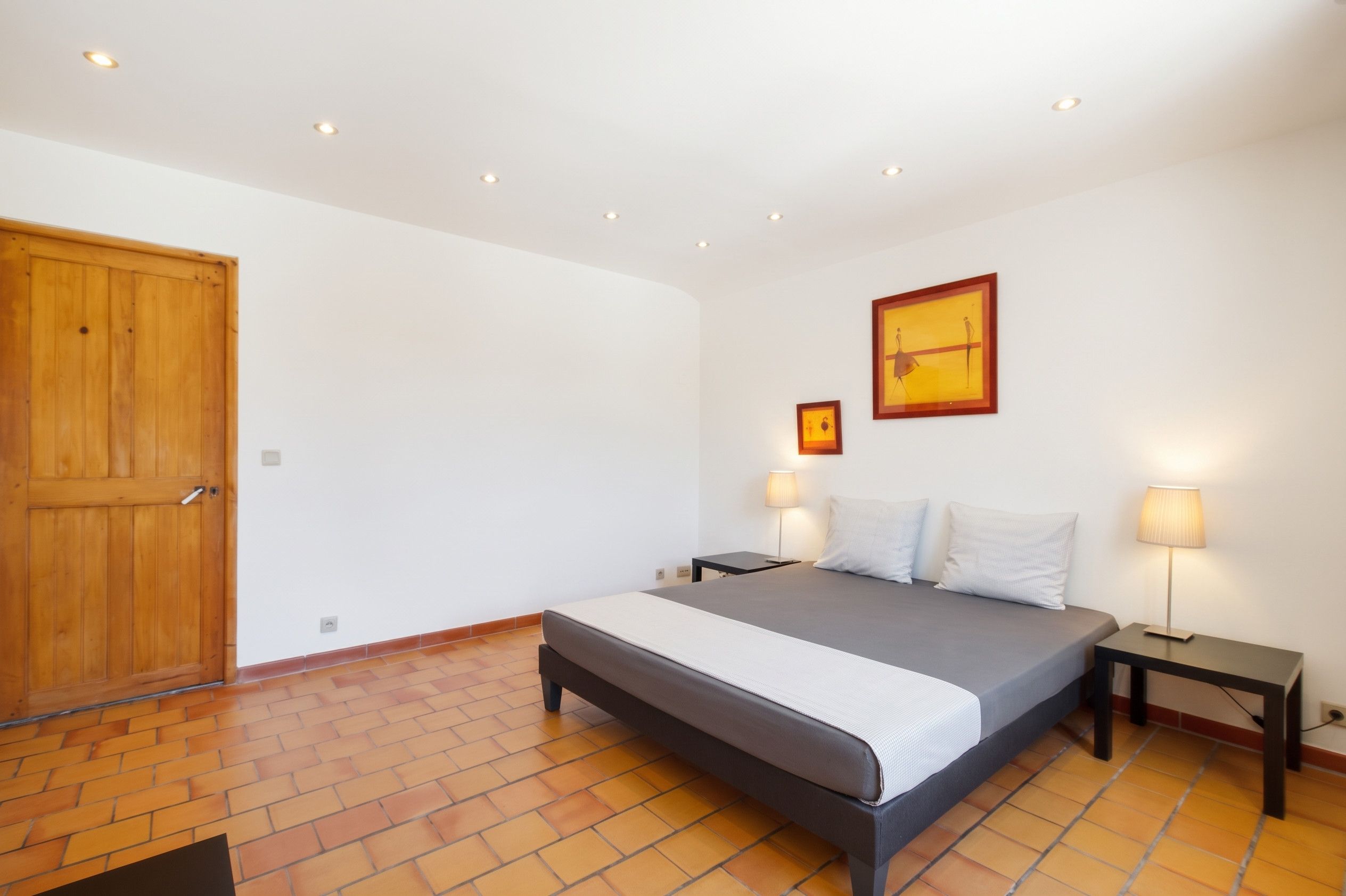 Ein Schlafzimmer mit einem Bett, zwei Nachttischen, einer Holztür und einem Fliesenboden.
