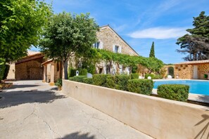 A stone building with a pool, surrounded by greenery and a clear sky.