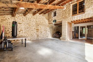 A spacious room with a stone wall, a ceiling with wooden beams, a punching bag, a table, and a bicycle.