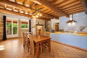 A spacious dining area with a wooden table and chairs, a kitchen with a blue backsplash, and a stone wall. - Homerez - Villa in Uchaux (Uchaux)