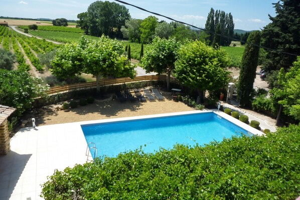 A swimming pool surrounded by lush greenery, with a view of vineyards in the background. - Homerez - Villa in Uchaux (Uchaux)